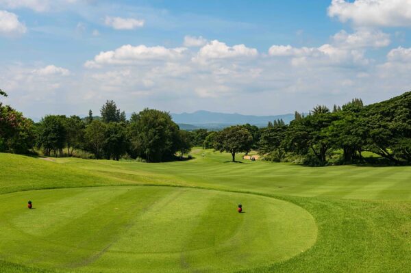 Banyan Golf Club i Hua Hin er en frodig grøn golfbane omgivet af majestætiske træer og høje bjerge i baggrunden. Det er et malerisk landskab