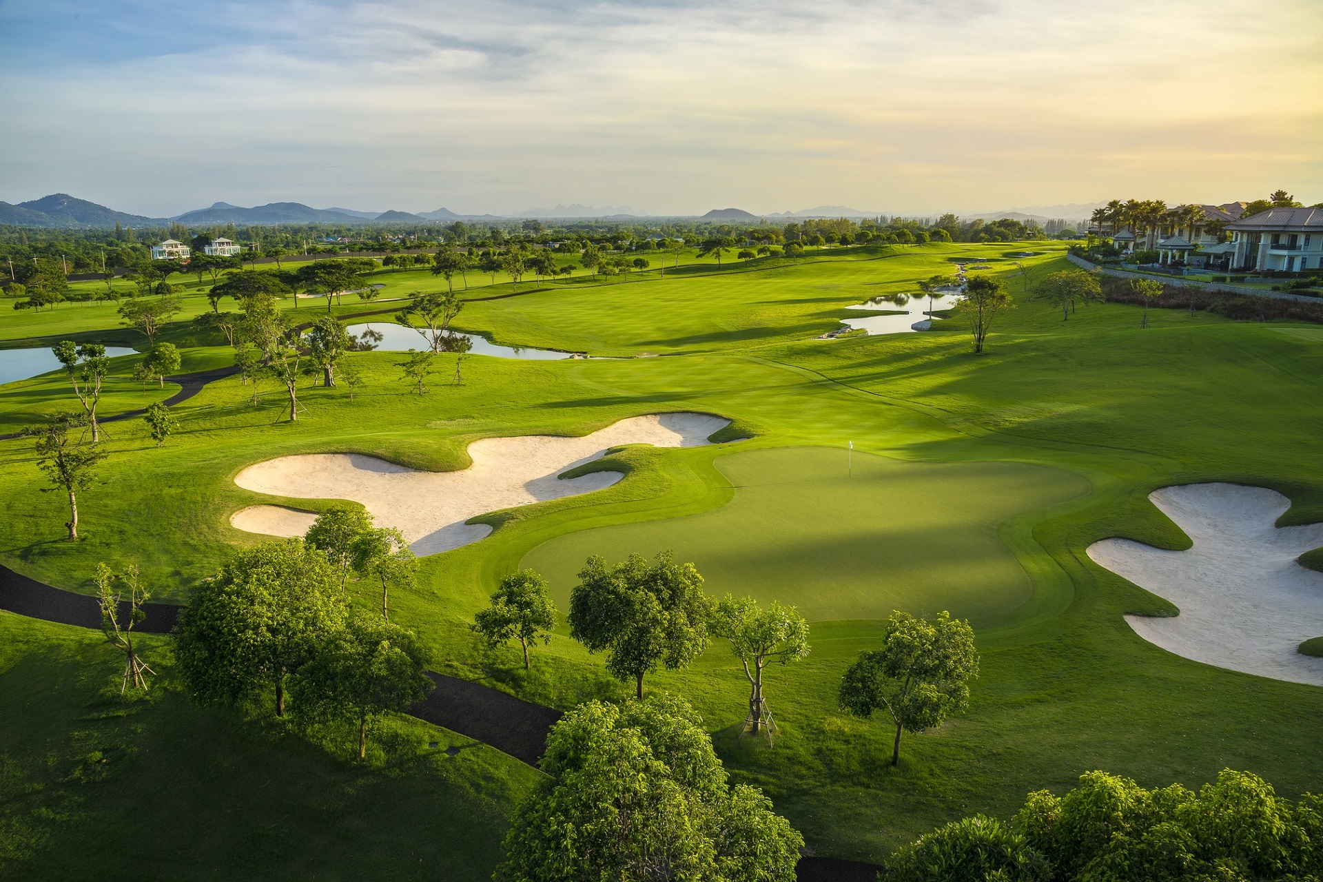 Overhead view af det grønne landskab og golfbaner på Black Mountain Golf Club, Hua Hin, Thailand. Billedet viser flere fairways omgivet af