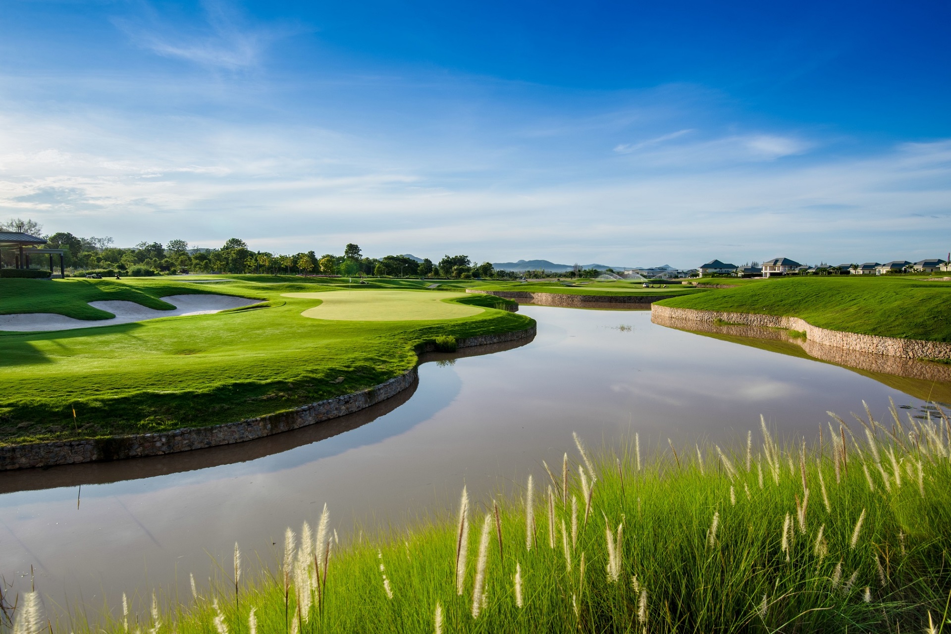 Se Black Mountain Golf Club i Hua Hin. Billedet viser en velholdt golfbane med grønt græs og vandfunktioner. Få et indtryk af golfbanens