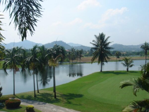 Burapha Golf og Resorts grønne golfbane med palmetræer omkring en smuk sø. Ideel for rejsende, der søger efter afslappende golfferiesteder i