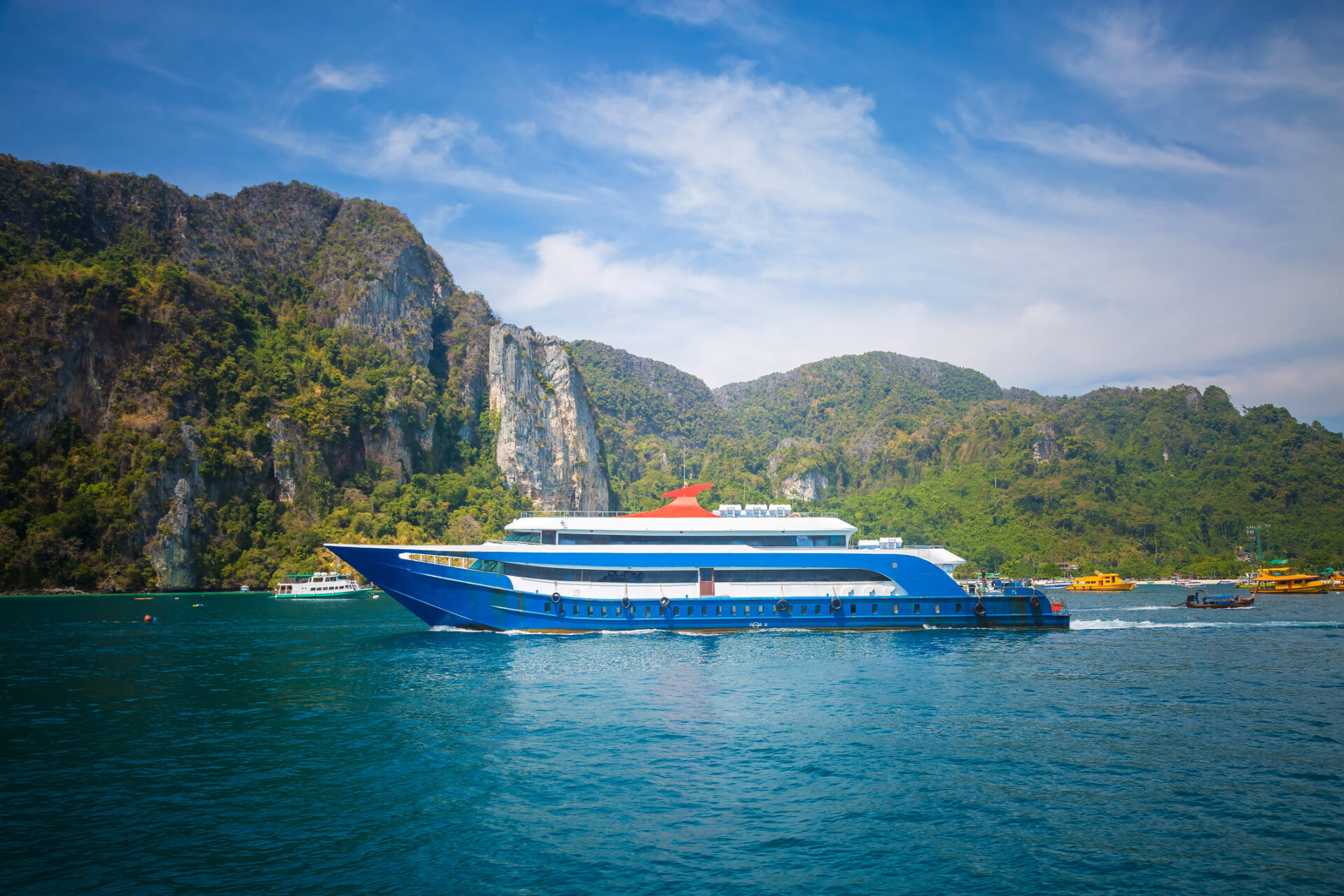 Traditionel thailandsk transportbåd i blå og hvid nær et bjerg i vandet