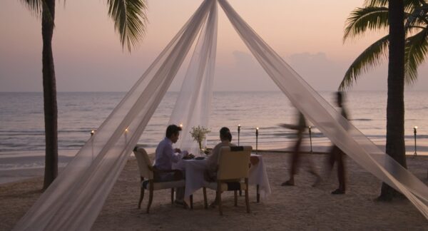 Personer sidder ved et bord på en strand om aftenen og nyder den rolige atmosfære i Hua Hin Resort & Spa.