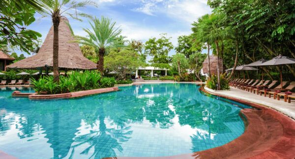 Anantara Hua Hin Resort swimmingpool omgivet af frodige træer og komfortable liggestole