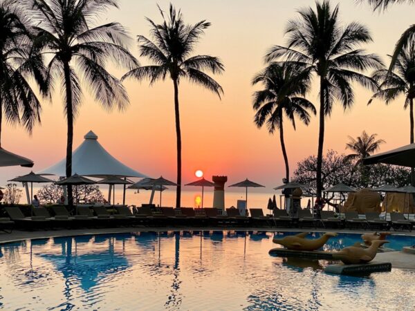 Solnedgangsudsigt over pool med liggestole på Hilton Hua Hin Resort & Spa omgivet af palmer