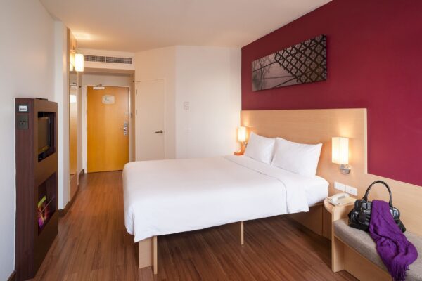 Røde vægge i et hyggeligt hotelværelse hos Riverside Ibis i Bangkok - rummet har en komfortabel seng klar til at byde dig velkommen efter en