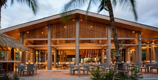 La Flora Resort Khao Lak ved skumring, viser restaurantområdet omgivet af palmetræer. På billedet ses silhuetterne af palmetræerne mod