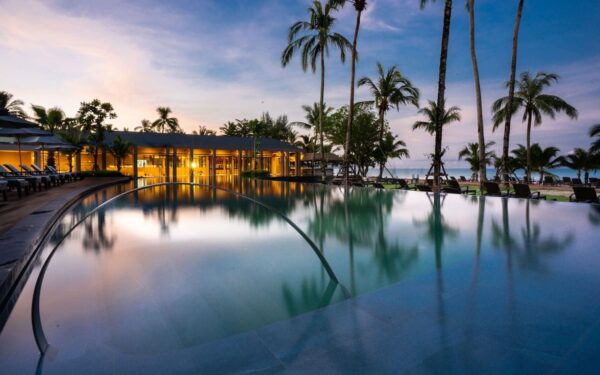 Swimmingpool omgivet af palmer på La Flora Resort Khao Lak i skumringen