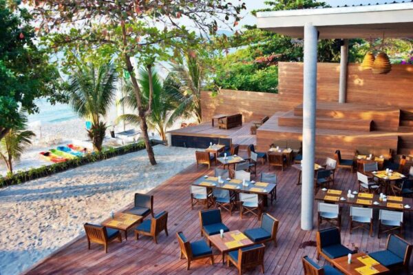 Sai Kaew Beach Resort restaurant med træborde og -stole på stranden.