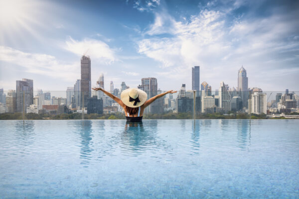 Kvinde med hat i swimmingpool med Bangkok skyline i baggrunden