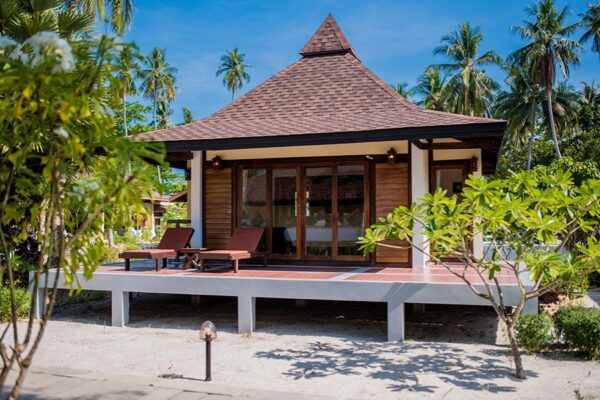 Træbungalow med spidst tag og glasdøre omgivet af palmer på sandet ved Sivalai Beach Resort, Koh Mook.
