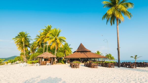Fredelig sandstrand med palmer, træhytter og udendørs café ved det klare hav på Sivalai Beach Resort, Koh Mook.
