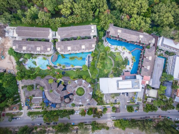 Overhead udsigt over et frodigt tropisk feriested i Thailand, der viser palmelandskab, swimmingpools, adgang til stranden og traditionel