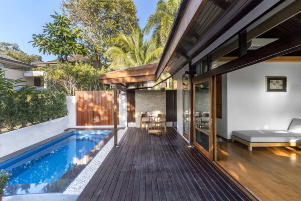 Elegant træterrasse med pool og glasfacade omgivet af frodig natur på et roligt resort i Thailand.