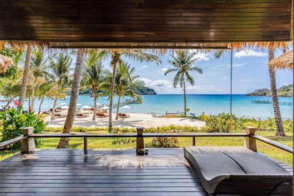 Træterrasse med liggestol og udsigt til palmer, hvide sandstrande og turkisblåt hav på en tropisk ø i Thailand.